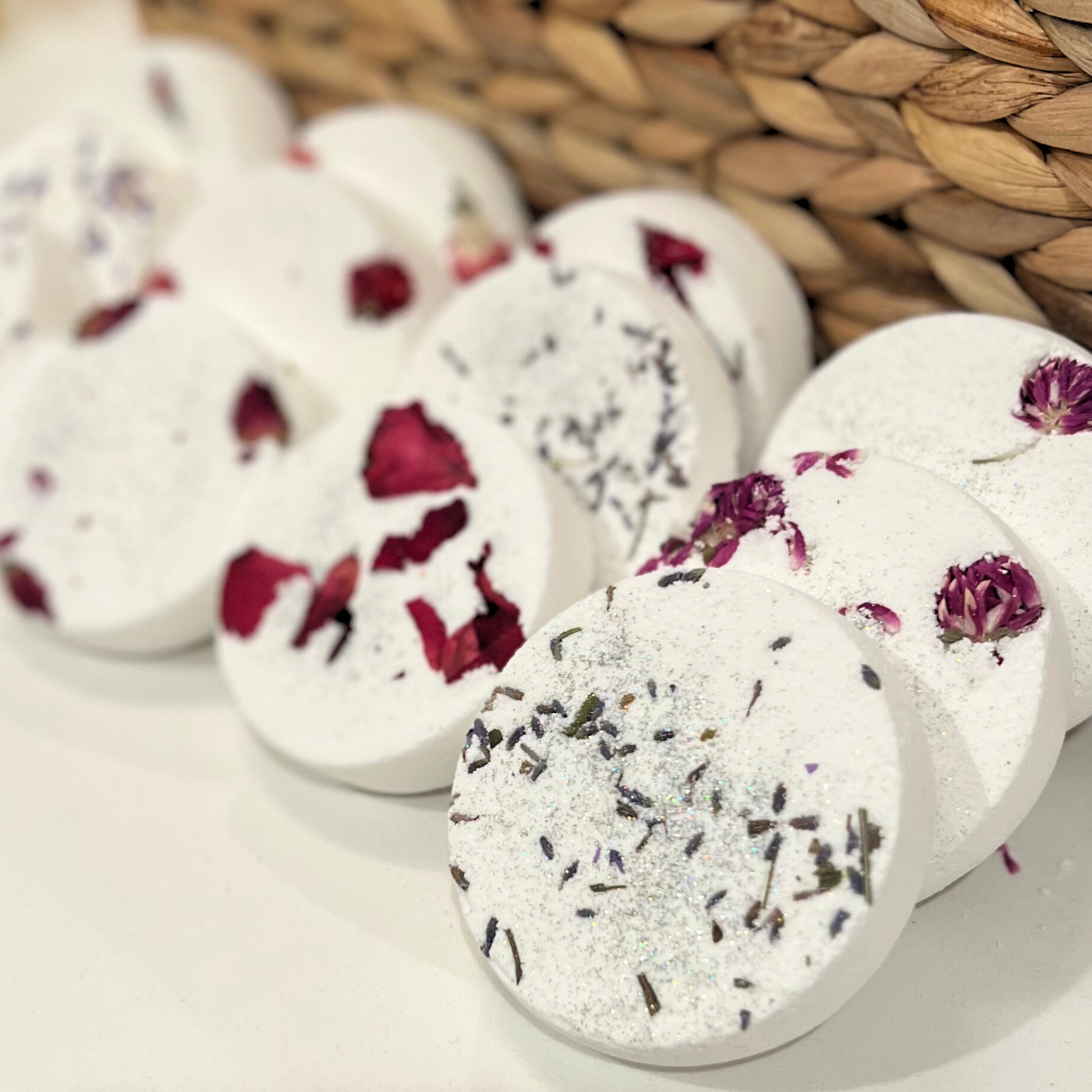 A collection of round shower steamers with embedded dried flowers and a woven background 