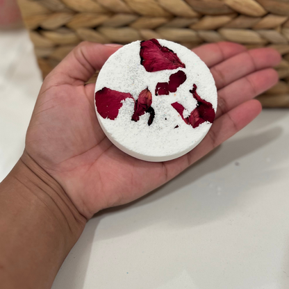 A hand holding a round shower steamer with dried rose flowers. 