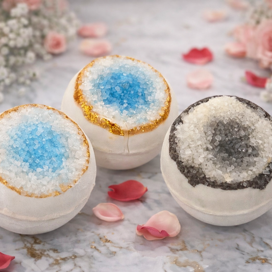 Three bath bombs with decorative coatings on a marble surface with flowers and petals.