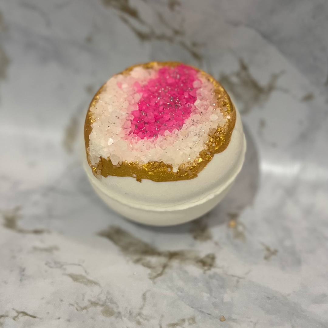 Bath bomb with pink center and gold top on a marble surface