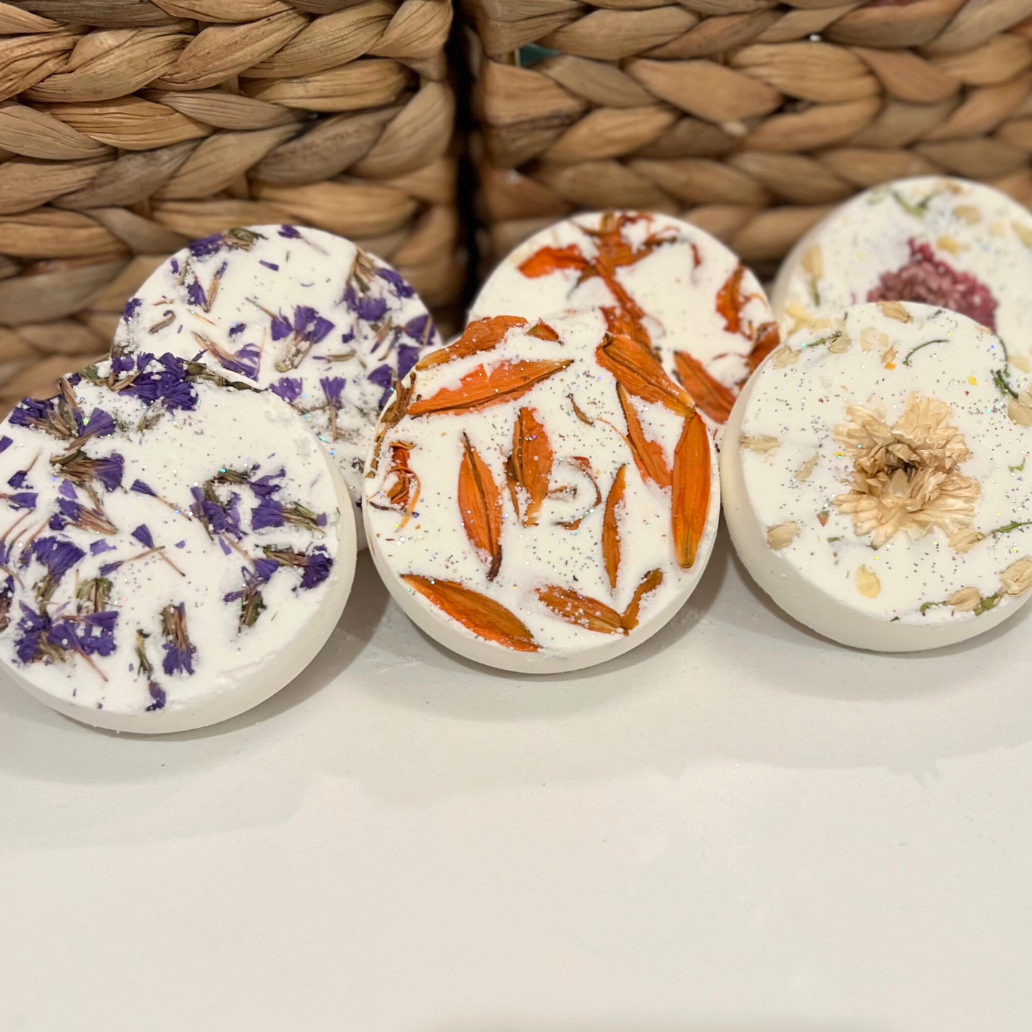 A collection of round shower steamers with embedded dried flowers and a woven background 