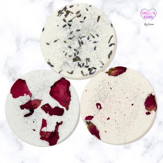 Three shower steamers in white, one with purple, and two with red dried flower toppings, displayed on a marble surface.