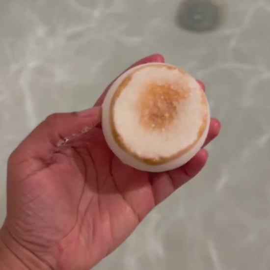 A video showcasing a bath bomb with a geode-inspired design, featuring a gold citrine-like structure on top with clear and gold hues, in the water fizzing. 