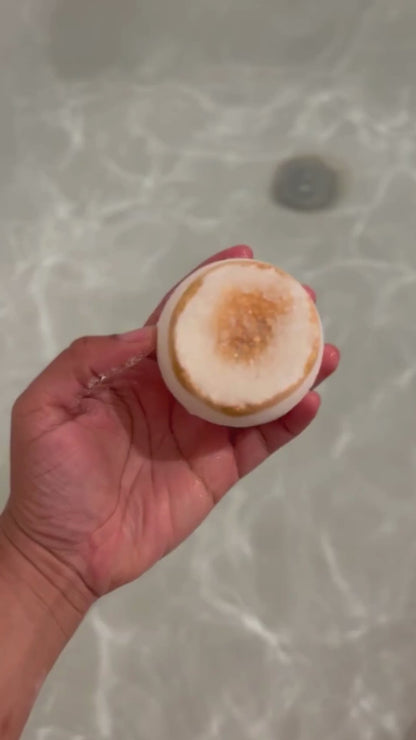 A video showcasing a bath bomb with a geode-inspired design, featuring a gold citrine-like structure on top with clear and gold hues, in the water fizzing. 