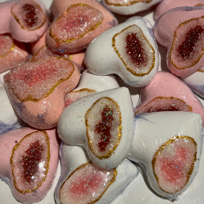 Multiple heart-shaped bath bombs with a geode-like pink center and red center with white exterior, adorned with biodegradable glitter along the edge.