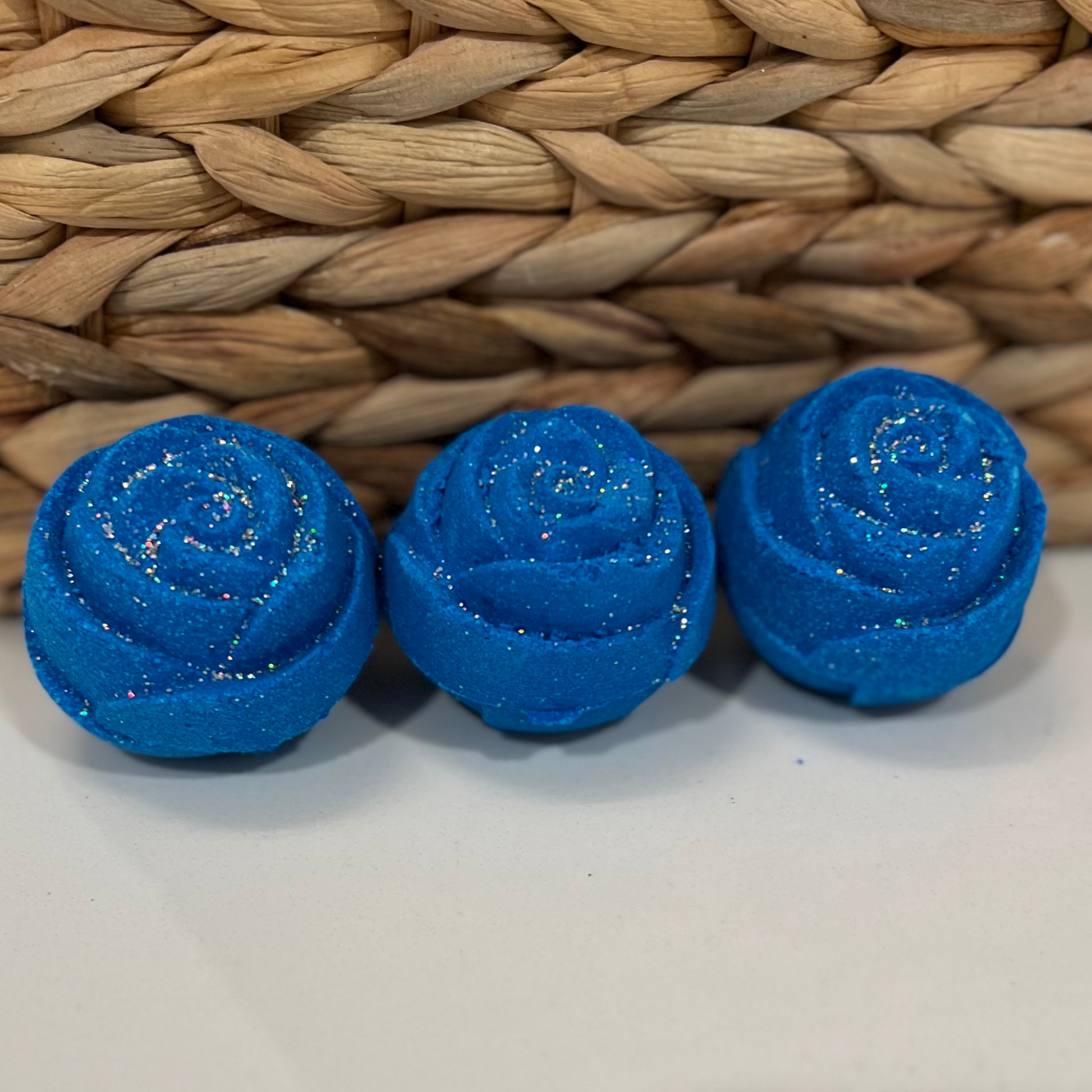 Three blue rose-shaped bath bomb with glitter, against a woven background.