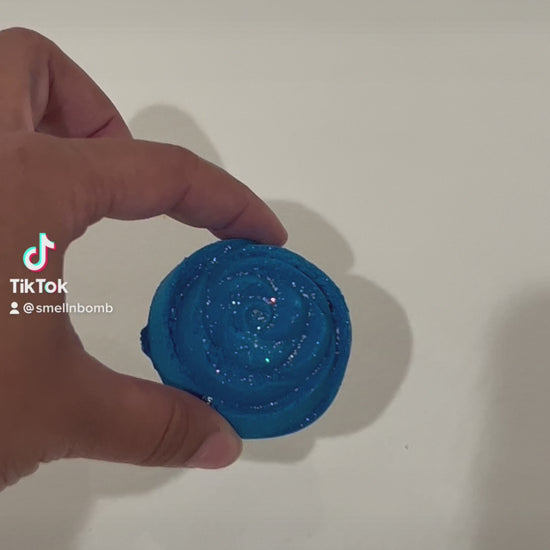 A video showing a blue rose-shaped bath bomb with glitter fizzing in the water.