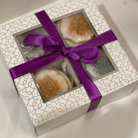 This gift set comes with four beautiful geode-inspired bath bombs. The gold geode-hue bath bombs are scented with our most popular fragrance, Love Spell, and the silver-hue geode bath bombs are scented with our second most popular scent, Pineapple Mango. It comes in a decorative white cardboard package that has a see-through window in the center and a ribbon tied around it. 